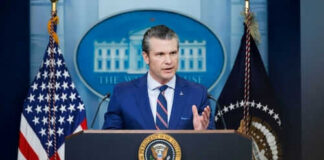 Man speaking at podium with flags in background