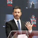 A man in a suit speaking at a podium during an event at TCL Chinese Theatre