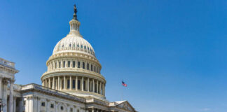 U.S. Capitol building with American flag, blue sky.