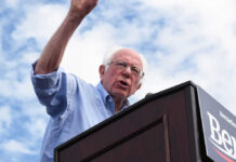 Man speaking at a podium under cloudy sky.