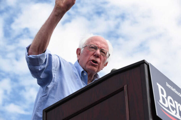 Man speaking at a podium under cloudy sky.