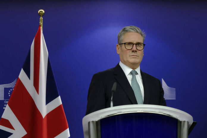 keir-starmer-751819750 Man in suit at a podium, British flag behind.