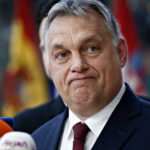 A political figure speaking at a press conference with microphones in front