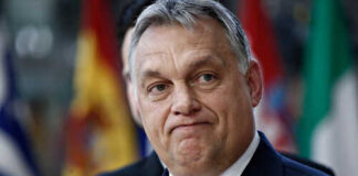 A political figure speaking at a press conference with microphones in front