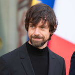 A man in a black suit smiling outdoors