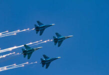 Four military jets flying in formation with smoke trails against a blue sky