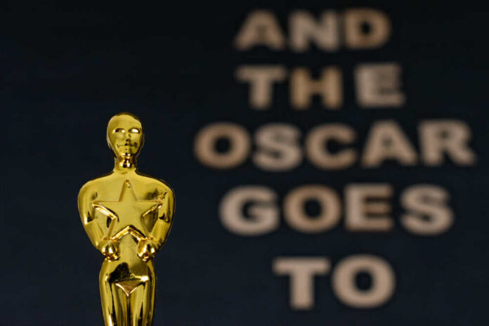 Close-up of an Oscar statue with the phrase 'And the Oscar goes to' in the background