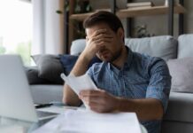 Man sitting in a home office looking stressed while reviewing paperwork