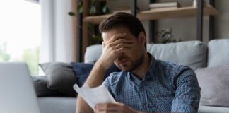 Man sitting in a home office looking stressed while reviewing paperwork