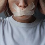 A person with tape over their mouth, symbolizing silence or oppression