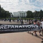 Two individuals holding a banner for reparations in front of the White House