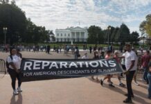Two individuals holding a banner for reparations in front of the White House