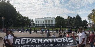 Two individuals holding a banner for reparations in front of the White House