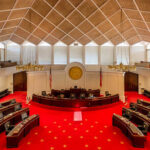 Interior view of a legislative chamber with red carpet and wooden accents