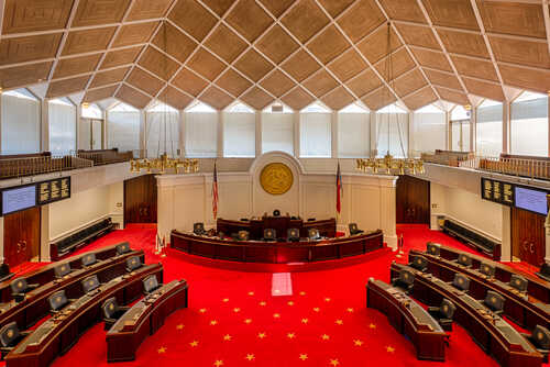 shutterstock_240133267.jpg Interior view of a legislative chamber with red carpet and wooden accents