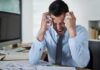 Frustrated businessman holding his head in an office filled with paperwork