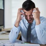 Frustrated businessman holding his head in an office filled with paperwork