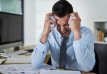 Shocking Most Stressed States: Not What You Think! Frustrated businessman holding his head in an office filled with paperwork