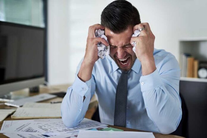 shutterstock_2482093919.jpg Frustrated businessman holding his head in an office filled with paperwork