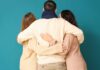 Three people embracing each other from behind against a teal background