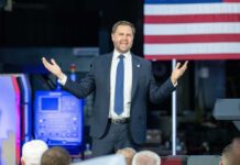 Vance’s Iran Shift: Betrayal or Strategy? A man in a suit passionately delivering a speech in front of an audience with an American flag in the background