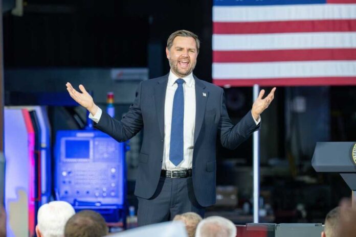 A man in a suit passionately delivering a speech in front of an audience with an American flag in the background