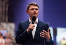 A man in a suit speaking into a microphone at a conference