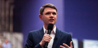 A man in a suit speaking into a microphone at a conference