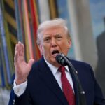 A man speaking passionately into a microphone with his hand raised