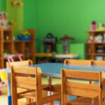 Brightly colored classroom with wooden tables and shelves filled with toys