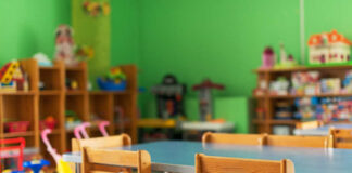 Brightly colored classroom with wooden tables and shelves filled with toys