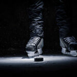 A pair of ice skates hovering above a hockey puck on the ice