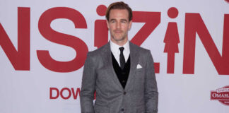 A man in a gray suit standing on a red carpet at a film premiere