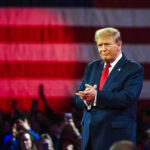 Person clapping in front of large American flag.