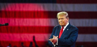 Person clapping in front of large American flag.
