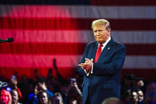 Person clapping in front of large American flag.