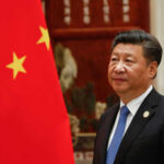 Man in suit standing next to Chinese flag