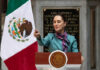 Person speaking at podium beside Mexican flag