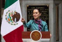 Person speaking at podium beside Mexican flag