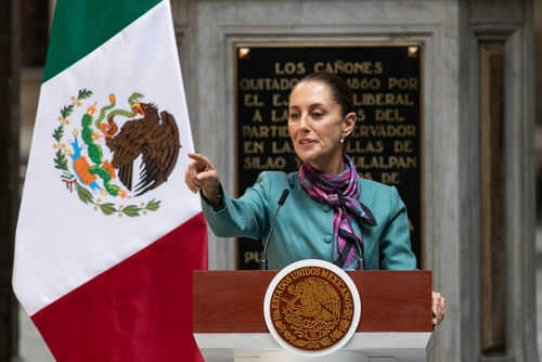 Person speaking at podium beside Mexican flag