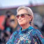 A woman wearing sunglasses and a colorful dress poses on the red carpet