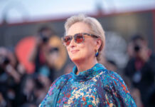 A woman wearing sunglasses and a colorful dress poses on the red carpet