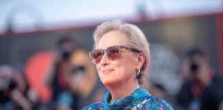 A woman wearing sunglasses and a colorful dress poses on the red carpet