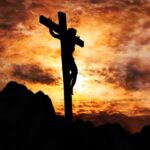 Silhouette of a crucifix against a dramatic sunset sky