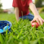 Child reaching for a red Easter egg on the grass