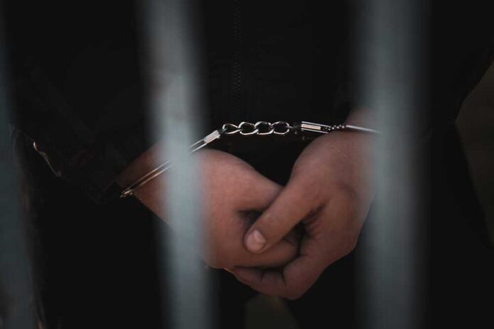 Close-up of handcuffed hands behind bars