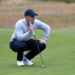 Golf Shock: McIlroy’s Lead Evaporates Golfer crouching on the green, preparing to putt