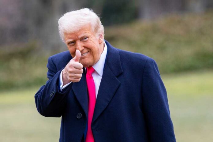 shutterstock_2589320069.jpg A man in a dark coat and pink tie giving a thumbs up outdoors