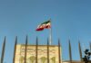 Iranian flag waving above a government building against a blue sky