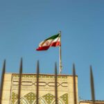 Iranian flag waving above a government building against a blue sky